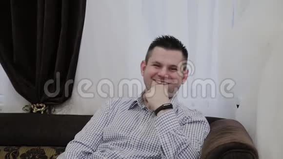 一个情绪化的男人坐在婚礼沙龙的沙发上对他的女人展示的衣服做出反应视频的预览图