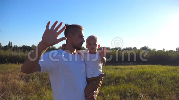 一家人在草地上挥舞着手臂对着镜头的肖像年轻的爸爸手牵着儿子的手视频的预览图