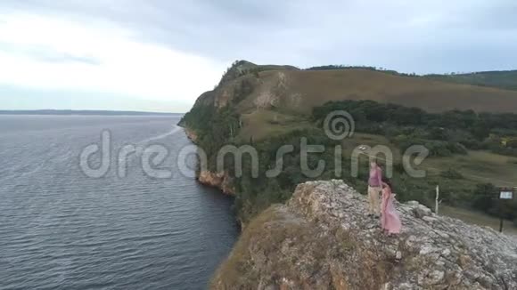 年轻夫妇站在海边的悬崖和岩石上的鸟瞰图视频的预览图