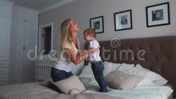 妈妈和儿子在一间明亮的卧室里的床上玩耍一个两岁的男孩笑了笑视频的预览图