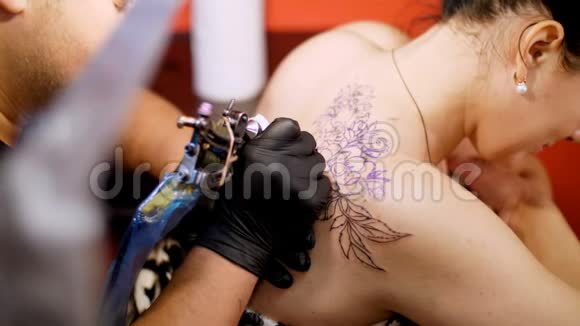 特写在一个纹身沙龙一位专家正在做一个纹身的女人背部黑色油漆花卉装饰一个人工作视频的预览图