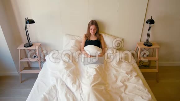 年轻的女士早上在床上从家里用笔记本电脑工作视频的预览图