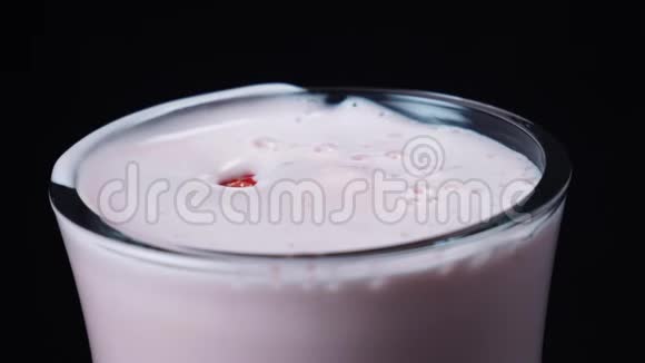 在黑色背景上用红色落下的大草莓装饰一杯清澈的草莓奶昔框架视频的预览图