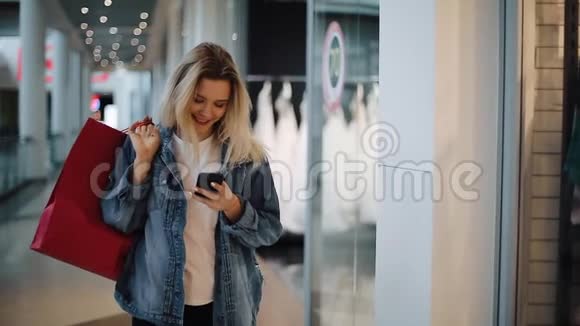 一个微笑的金发女孩在手机里读到一些东西她带着购物袋在购物中心走来走去视频的预览图