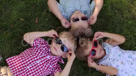 三个戴太阳镜的孩子在草地上的肖像视频的预览图