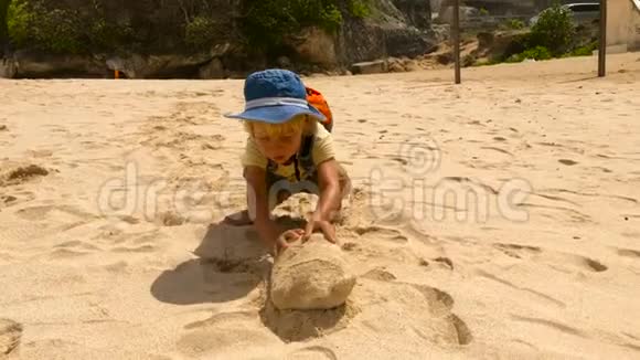 印度尼西亚巴厘岛上一个顽固不化的小男孩推着一块大石头在海浪滚滚的海滩上视频的预览图