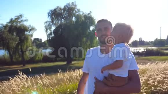 在阳光明媚的日子里一家人在草地上的画像年轻的爸爸在田里双手抱着他的孩子父亲和视频的预览图