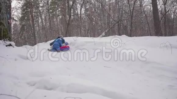 两个孩子坐在雪山上的雪橇上孩子们用雪橇摔倒体育和户外活动视频的预览图