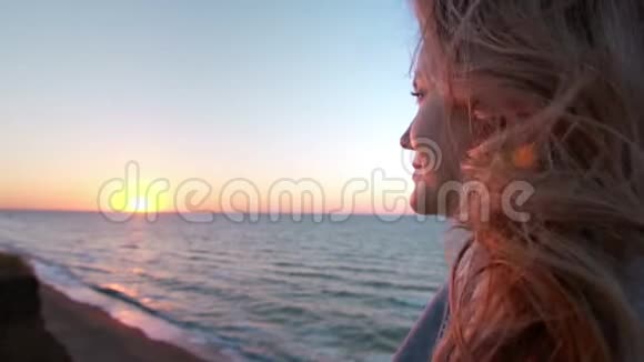 美丽的白种人卷曲的金发年轻女子在日出或日落海边风发了头发概念视频的预览图
