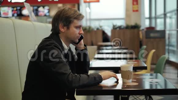 室内拍摄的微笑年轻人坐在咖啡店和手机交谈咖啡馆里的快乐小伙子视频的预览图