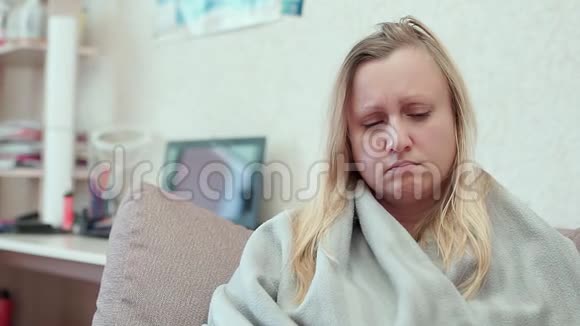 一个女人看着医用温度计坐在沙发上的毯子视频的预览图