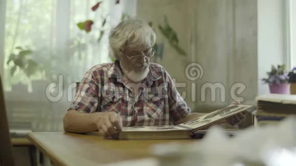 老人坐在家里看着他的旧专辑和照片视频的预览图
