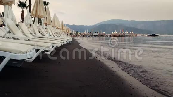 日落后海滩上的空晒床和平静的海浪的4k镜头视频的预览图