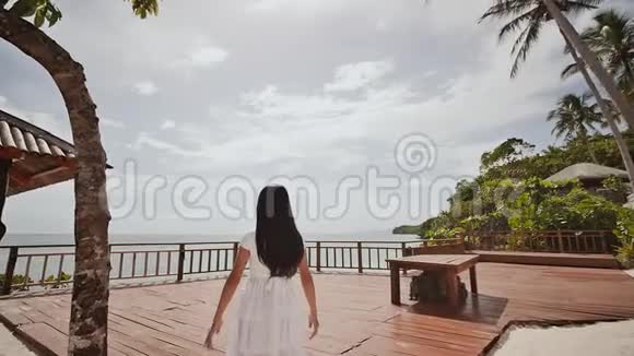 一个迷人的菲律宾女学生穿着白色的裙子在一个高台俯瞰海洋可怕的高度和钦佩视频的预览图