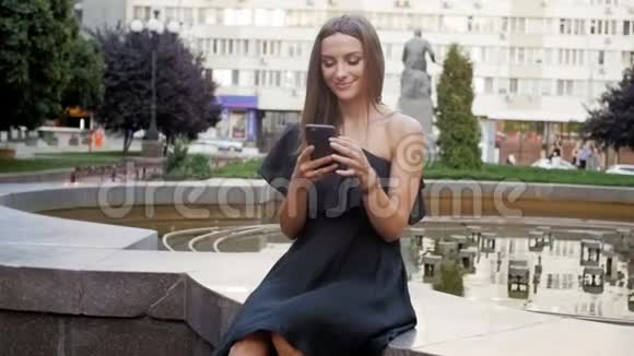坐在喷泉旁用智能手机的美女慢动作视频视频的预览图