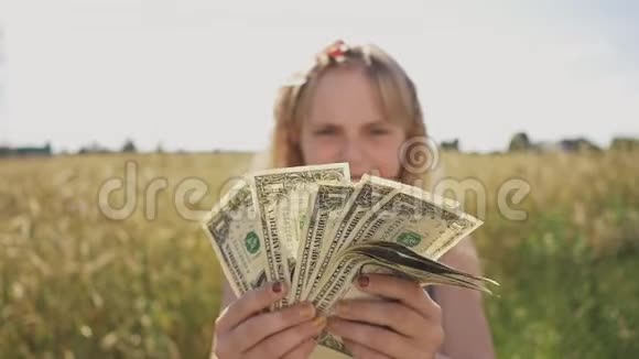 一个美丽的小女孩在一个温暖阳光的日子里拿着钱在大自然的背景下金钱财政和视频的预览图