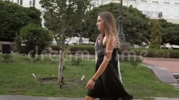 穿着黑色短裙的时髦年轻女子在公园散步的慢动作视频视频的预览图
