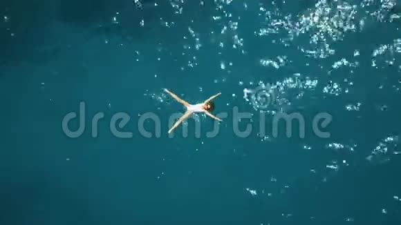 一位身穿白色泳衣在碧海中沐浴的年轻美女的高空俯视图视频的预览图