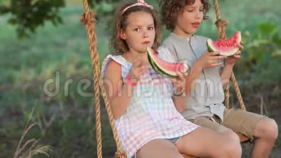 学生们在度假孩子们坐在秋千上吃西瓜女孩吐出种子视频的预览图