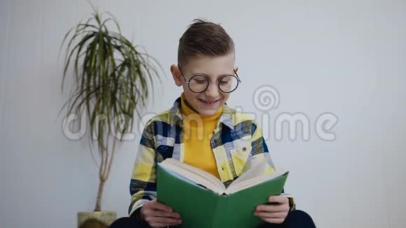 一个戴着蓝眼睛眼镜的迷人小男孩在家读一本有趣的书坐在白墙旁边的学生读视频的预览图