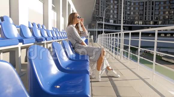 在体育场空座位上放松的时尚年轻女性慢动作视频视频的预览图