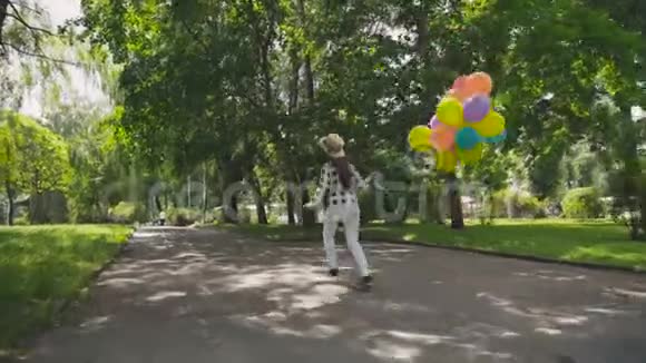 年轻女孩在绿色公园奔跑的背影手里拿着五颜六色的气球视频的预览图