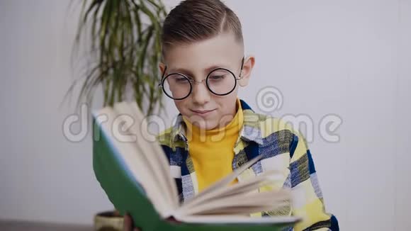 六七岁的男孩戴着成人眼镜看书白种人男孩坐在地板上看课本有饮料视频的预览图