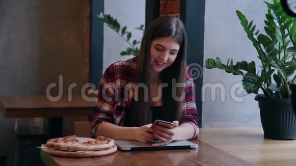 漂亮迷人的商务女性坐在咖啡馆的桌子上拿着手机和笔记本电脑桌子上有披萨视频的预览图
