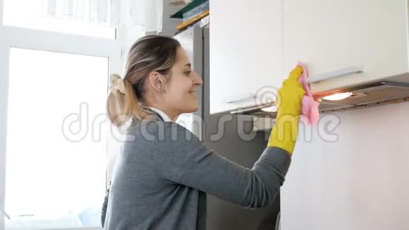 4k视频微笑的年轻女子戴着乳胶手套用布清洁厨房的橱柜视频的预览图