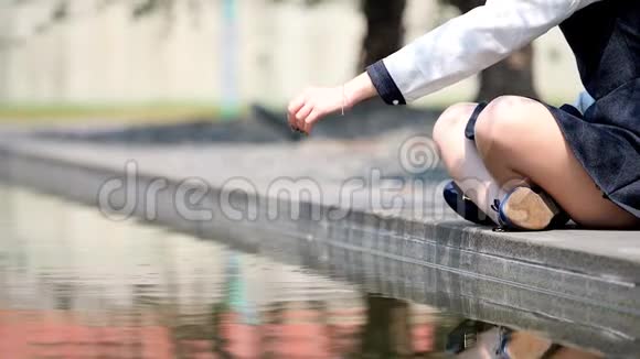 女孩坐在池塘的边缘在阳光明媚的夏日把一颗鹅卵石扔进平静的水中超级慢动作电影视频的预览图