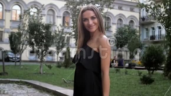 一个美丽的微笑女人穿着黑色衣服在公园里散步和看镜头的慢动作视频视频的预览图