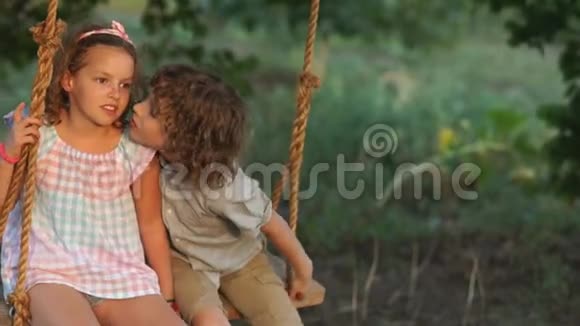 可爱的男孩和女孩坐在彼此旁边的秋千上男孩吻了女孩她打了他的脸颊视频的预览图