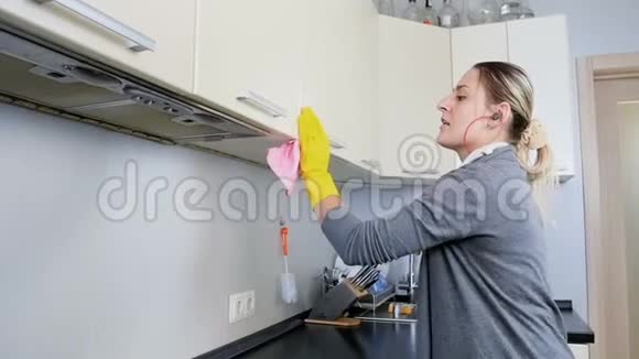 快乐的年轻家庭主妇在清洗厨房时用耳机听音乐的慢动作视频视频的预览图