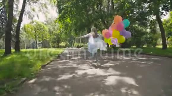 年轻女孩在绿色公园奔跑的背影手里拿着五颜六色的气球视频的预览图