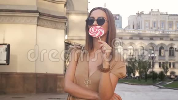 时尚年轻女性在街上舔大棒棒糖的慢镜头视频的预览图