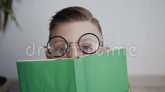 小男孩用一本书合上了脸他有一双蓝眼睛戴着眼镜孩子微笑着看着视频的预览图