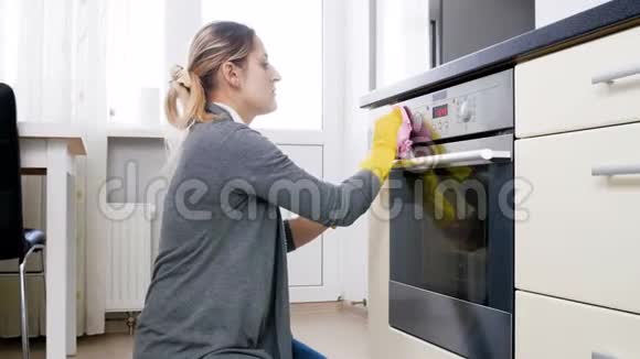 年轻微笑的家庭主妇清洁厨房电烤箱玻璃门的录像视频的预览图