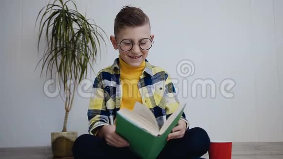 这个戴眼镜的小男孩在白色的室内地板上坐着一边读着有趣的书学生读视频的预览图