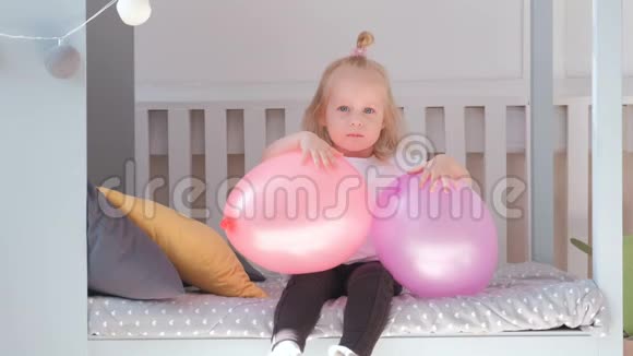 小可爱的金发女孩坐在她房间里的床上带着粉红色的气球微笑着视频的预览图