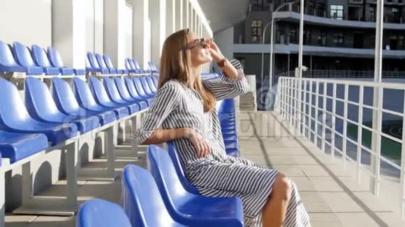 4K镜头时尚年轻女子在阳光明媚的一天在空旷的体育场放松视频的预览图