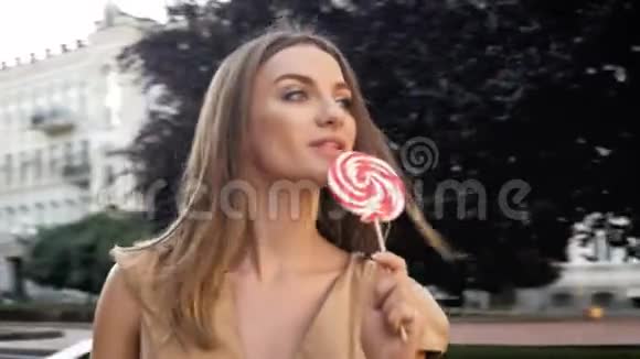 特写4k镜头快乐的年轻女子走在街上舔棒棒糖视频的预览图