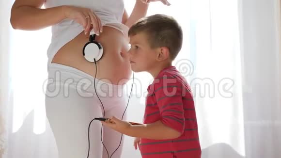 手里拿着android的孩子把耳机放在孕妇肚子上婴儿肚子里听音乐视频的预览图