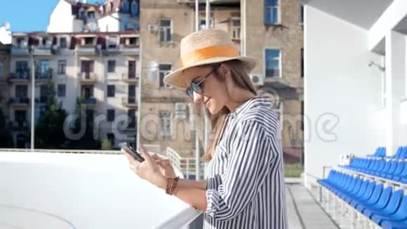 街头使用智能手机的时尚微笑女人戴帽子和太阳镜4k镜头视频的预览图