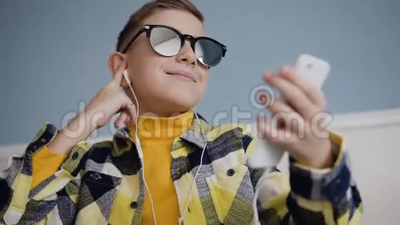 一个戴墨镜的金发男孩的特写镜头他戴着耳机听音乐还在跳舞点头视频的预览图
