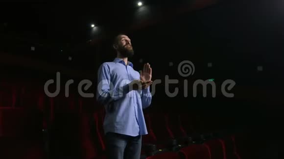 单身男子坐在黑色电影院舒适的红色椅子上鼓掌视频的预览图