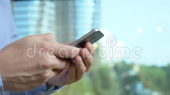 特写镜头男人的手在窗户的背景下使用电话从窗户上可以看到摩天大楼视频的预览图