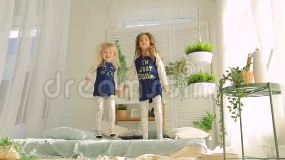 在明亮的房间里两个小女孩在床上跳着绿色的植物视频的预览图