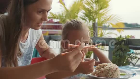 年轻的妈妈教她可爱的小女儿用筷子吃饭视频的预览图