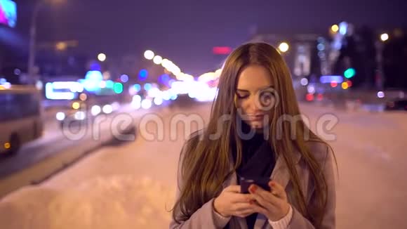 可爱的快乐女人微笑着在智能手机上写着一条信息站在城市的近旁交通视频的预览图