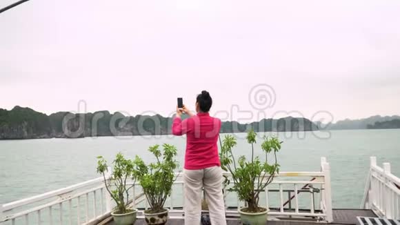 穿粉红色夹克的女人拍照这位女士乘旅游船在越南一个美丽的海湾附近旅行这就是视频的预览图